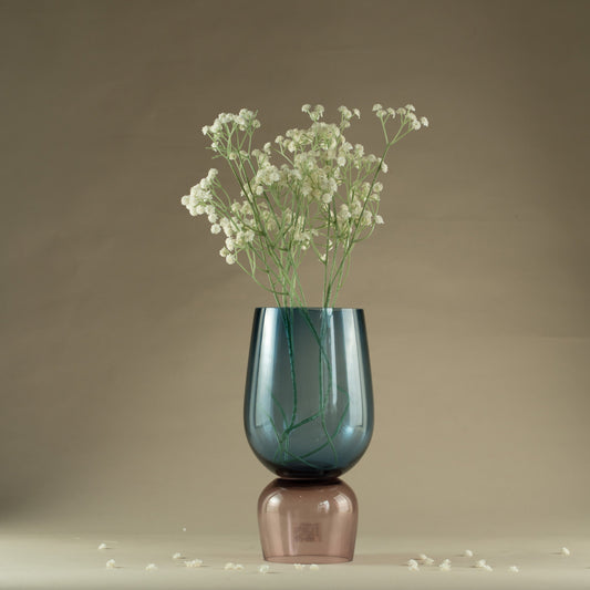 Blue glass vase with a pink base containing small white flowers on a neutral background