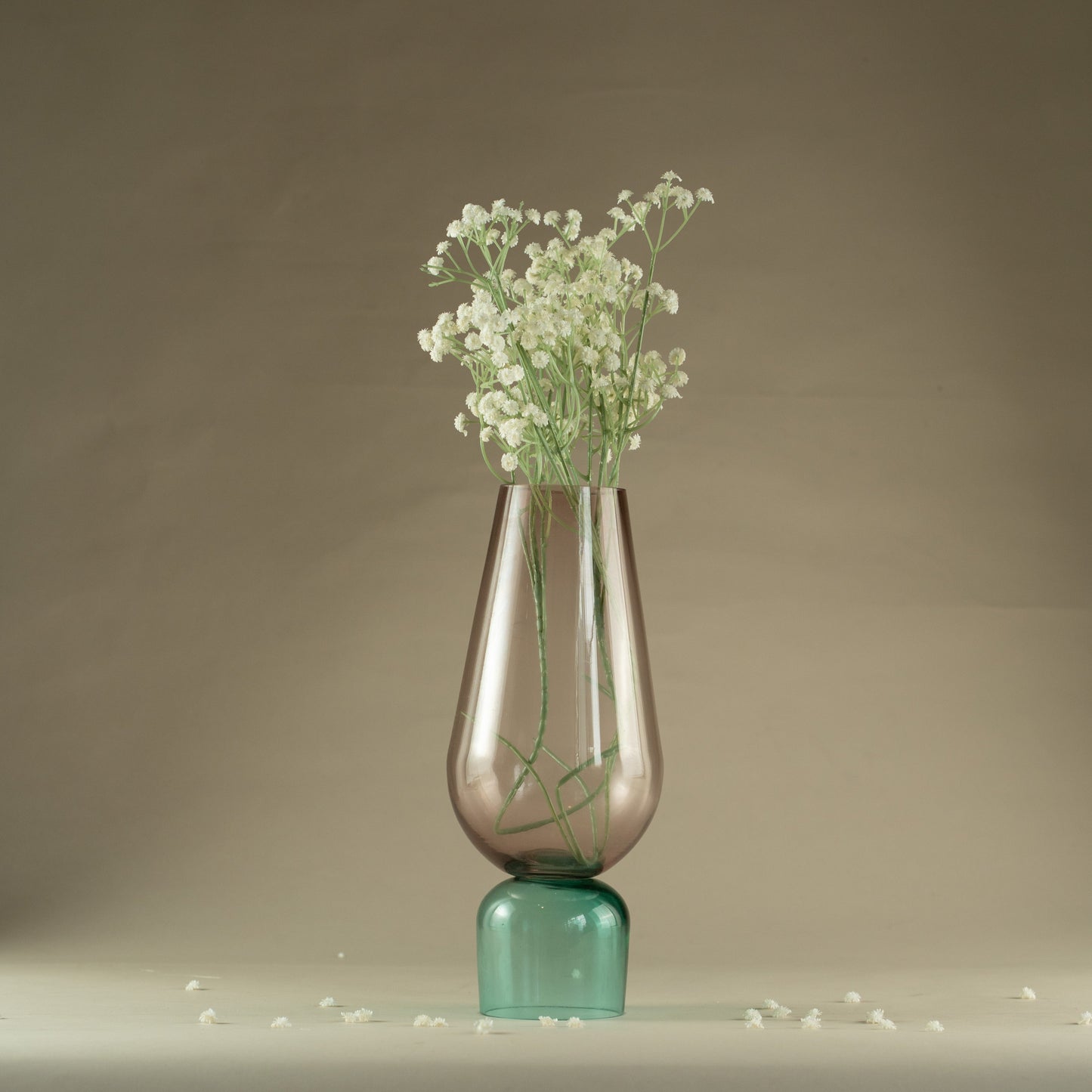 Clear glass vase with green base containing small white flowers on a neutral background
