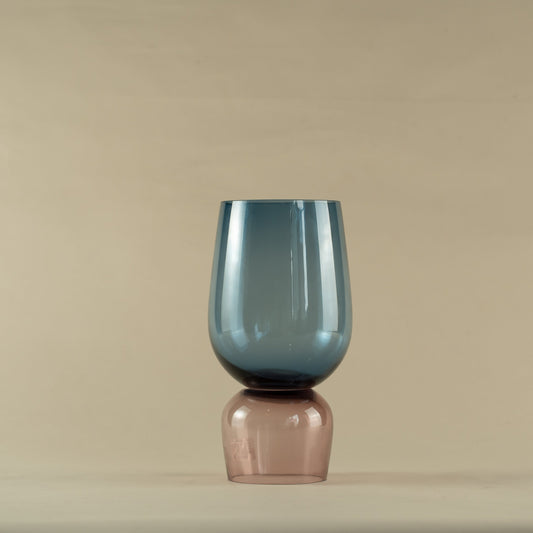 Blue glass vase with a pink base containing small white flowers on a neutral background