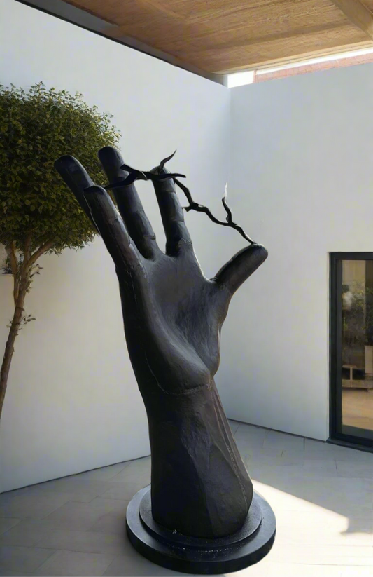 Large black hand sculpture in an outdoor setting with a tree and building in the background.
