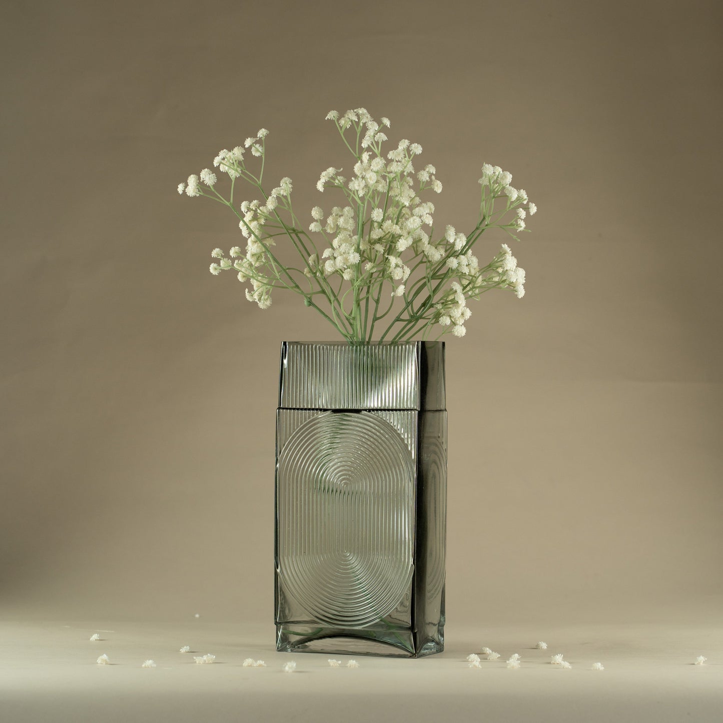Glass vase with small white flowers on a neutral background