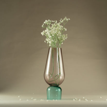 Clear glass vase with green base containing small white flowers on a neutral background
