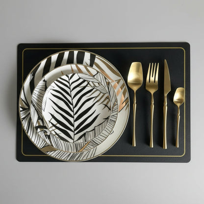 Dinner set with zebra-patterned plate, gold cutlery, and black placemat on a gray surface.