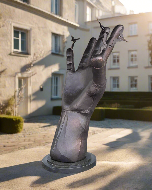Large black hand sculpture in an outdoor setting with a tree and building in the background.