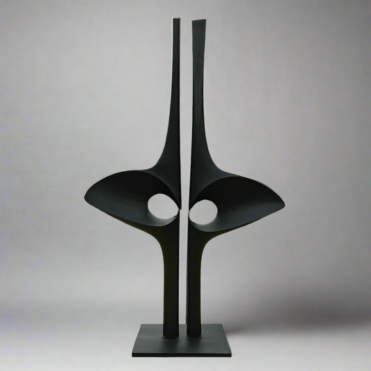 Modern black sculpture in front of a house with trees in the background